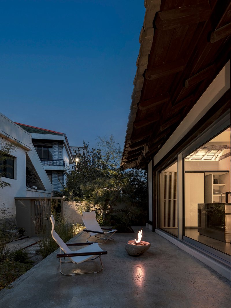 Courtyard terrace at dusk with fire bowl, lounge chairs and timber eaves above glazed walls