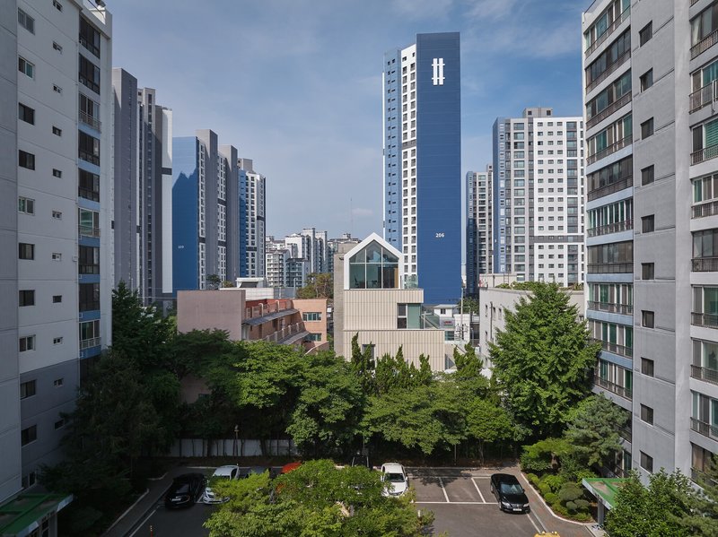 Courtyard view of a white house with gabled roof nestled among residential towers and greenery