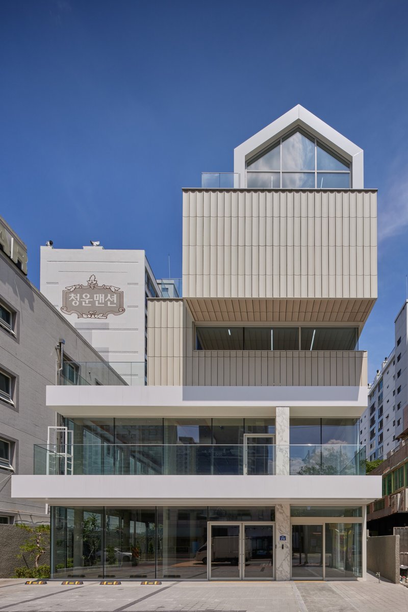 Street facade with stacked volumes of corrugated metal panels and glazed lower levels under clear sky