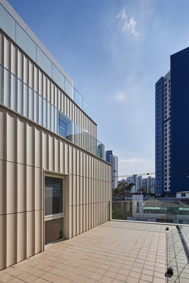 Rooftop terrace with vertical metal cladding and tiled paving framed by residential towers
