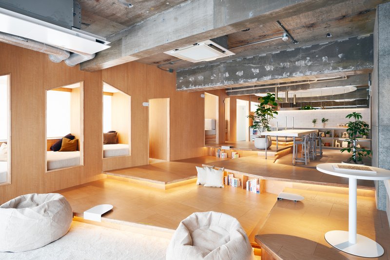Open-plan interior with sunken plywood platform seating and exposed concrete ceiling beams