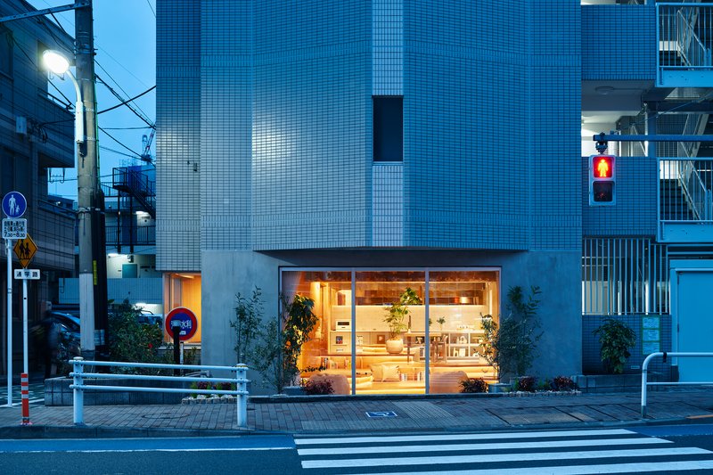 Street view of illuminated storefront with glass facade at dusk beside a crosswalk