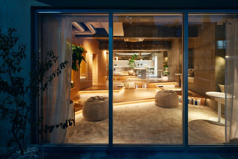 Exterior view at dusk showing the illuminated interior through full-height glazed sliding doors with a climbing plant to the left