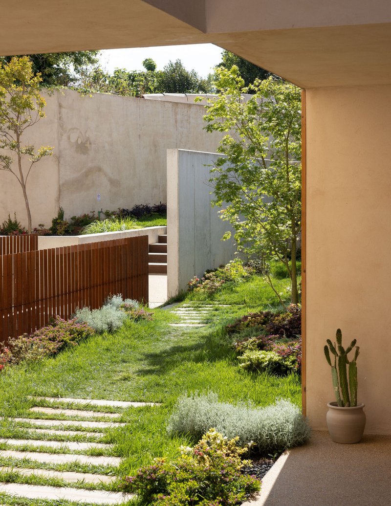 Garden courtyard view through arched opening with stepping stone path and timber slatted screen wall beyond
