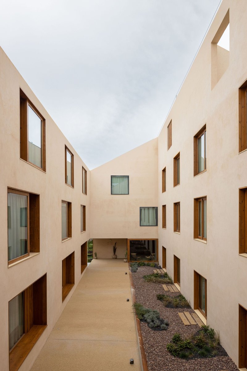 Internal courtyard with cream plaster walls, timber-framed windows and gravel beds with low plantings