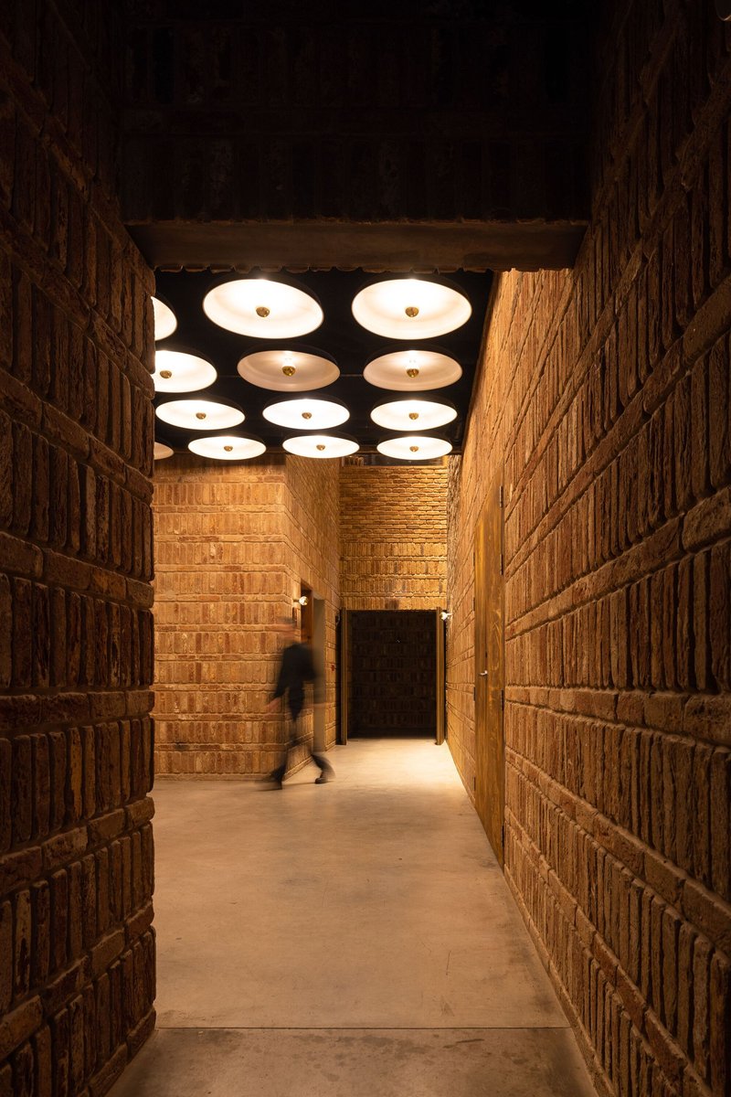 Corridor with textured brick walls and circular ceiling lights illuminating a figure passing through