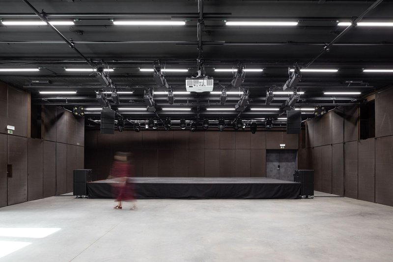 Performance hall with exposed ceiling lighting grid, dark timber wall panels, and a figure in motion