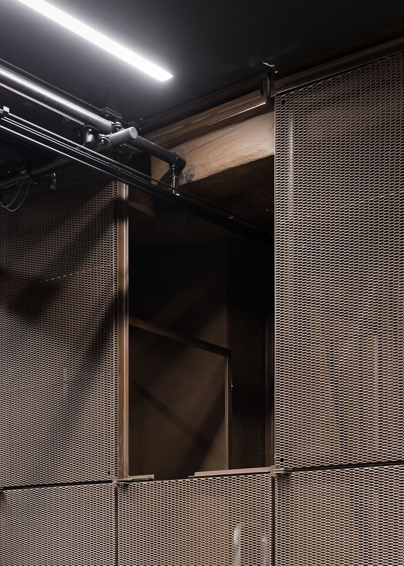 Detail of metal mesh panels meeting timber framing with track lighting overhead