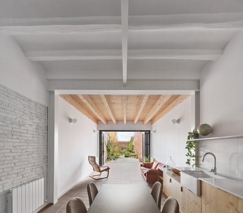 Interior view through dining and kitchen spaces toward the folding glass doors and planted courtyard beyond