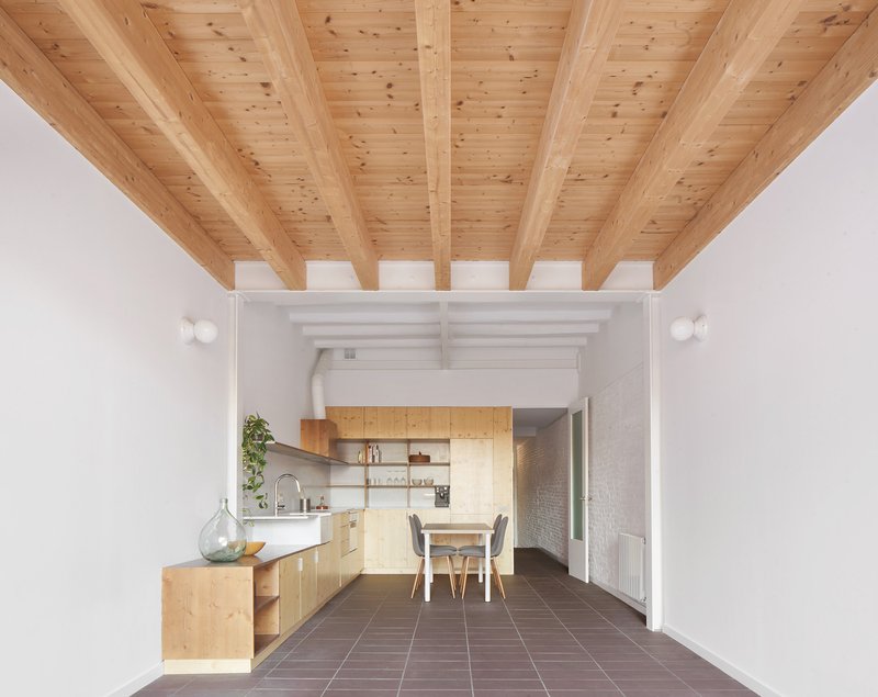 Open-plan kitchen and dining space with exposed timber beams, plywood cabinetry, and terracotta floor tiles