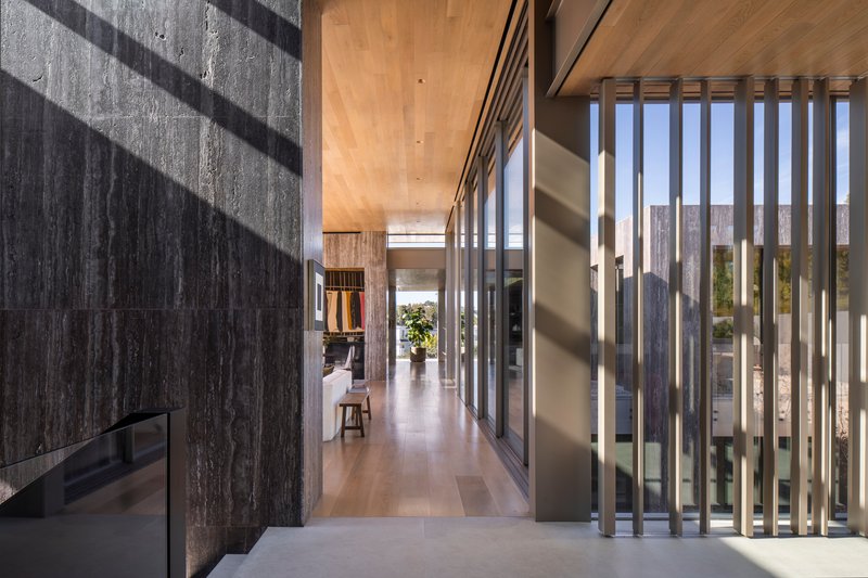 Interior corridor with board-formed concrete wall and timber ceiling flanked by vertical metal screen