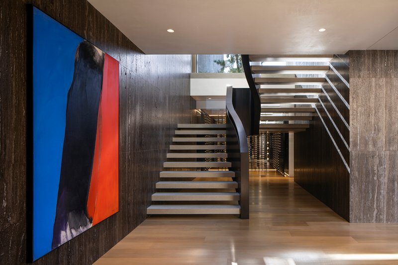 Open-tread staircase with steel stringers ascending beside a board-formed concrete wall and colorful canvas