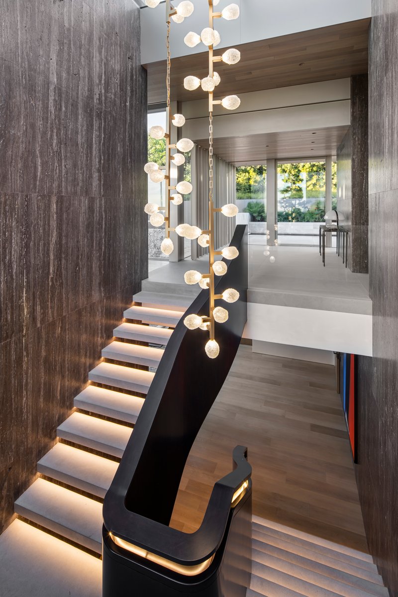 Curved black staircase with integrated LED lighting beneath each tread and a cascading globe pendant above