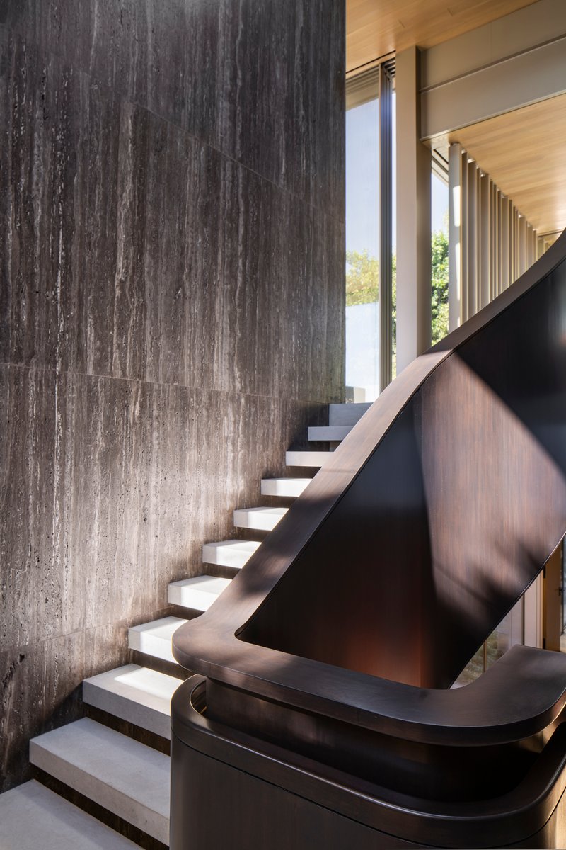 Detail of the sculptural staircase with black metal balustrade against a board-formed concrete wall