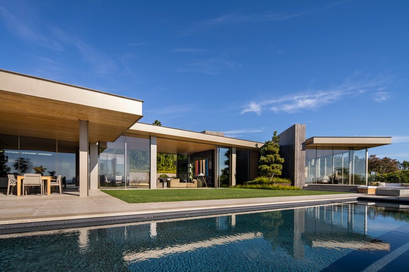 Garden facade with extended roof overhangs and glass walls opening to a lawn and swimming pool