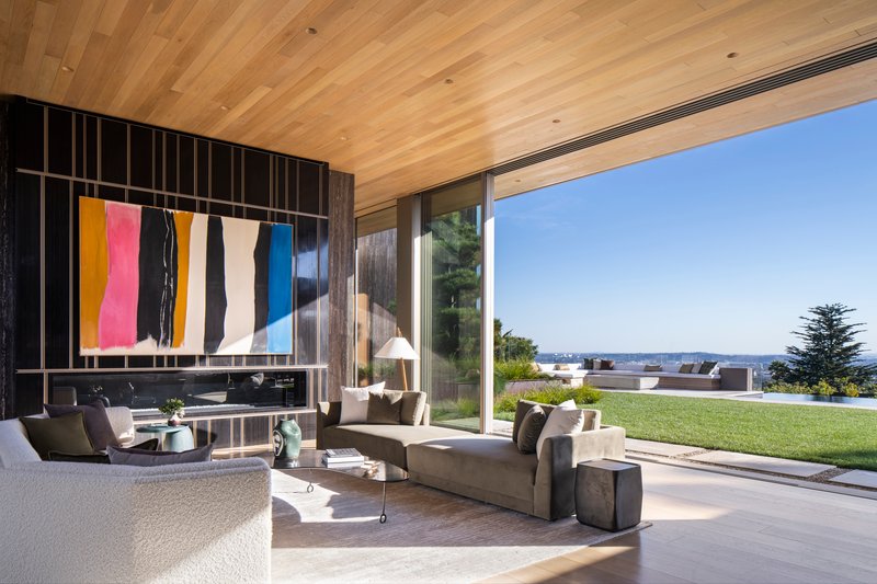 Living room with diagonal wood ceiling, dark metal wall screen, and full-height glazing to the garden