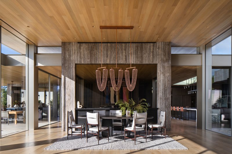 Covered dining area with timber ceiling, weathered wood-clad columns, and chandelier above a round table
