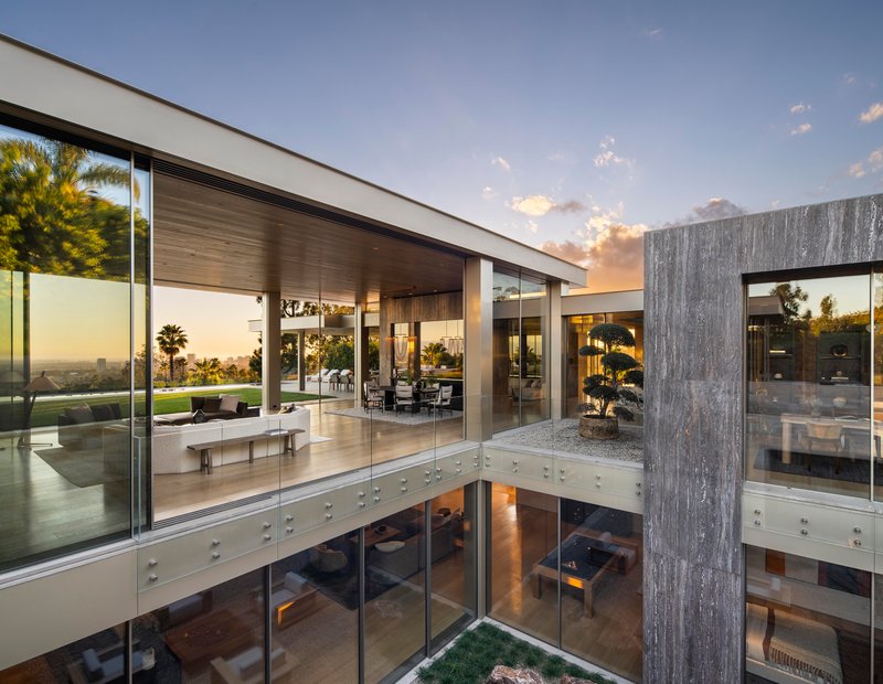 Double-height courtyard with glass-wrapped volume and weathered concrete tower at dusk