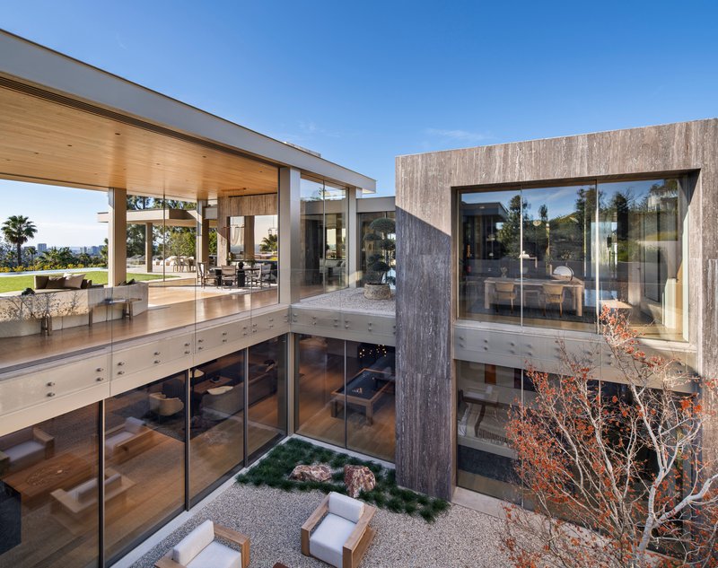 Sunken courtyard with planted bed and weathered concrete column beneath glazed upper floor terrace