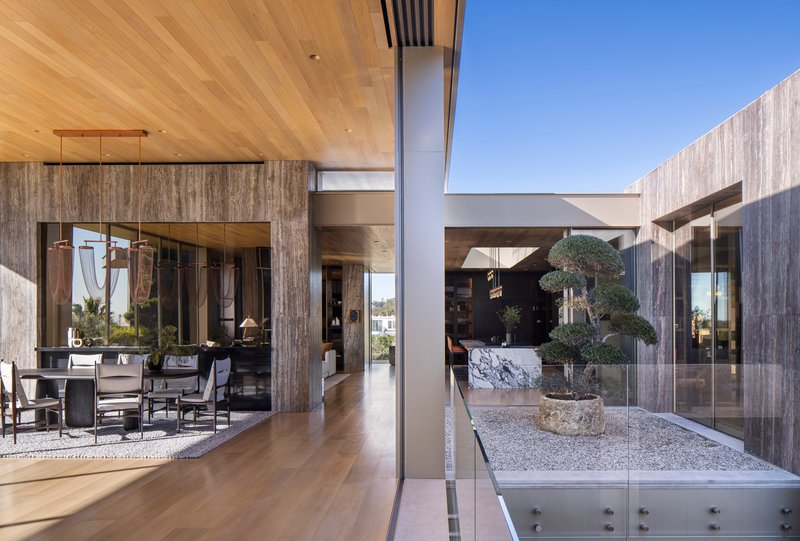 Central courtyard with gravel bed, sculptural tree in stone planter, and timber-clad volumes surrounding it