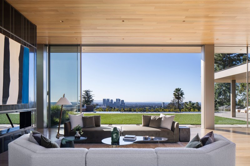 Living room with corner glazing framing lawn and distant skyline view beyond curved seating