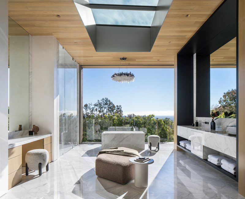 Bathroom with central marble tub, skylight above, and glazed wall opening to hillside vegetation