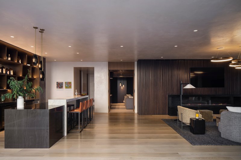 Open-plan living area with dark wood wall panels, stone bar island, and recessed ceiling lighting