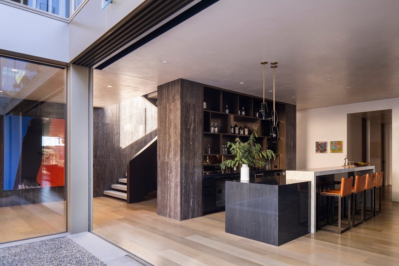 View from exterior threshold showing kitchen bar, sculptural staircase, and full-height glazed sliding doors