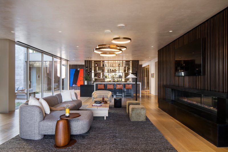 Living room with ring pendant lights, grey upholstered seating, and linear fireplace in dark millwork