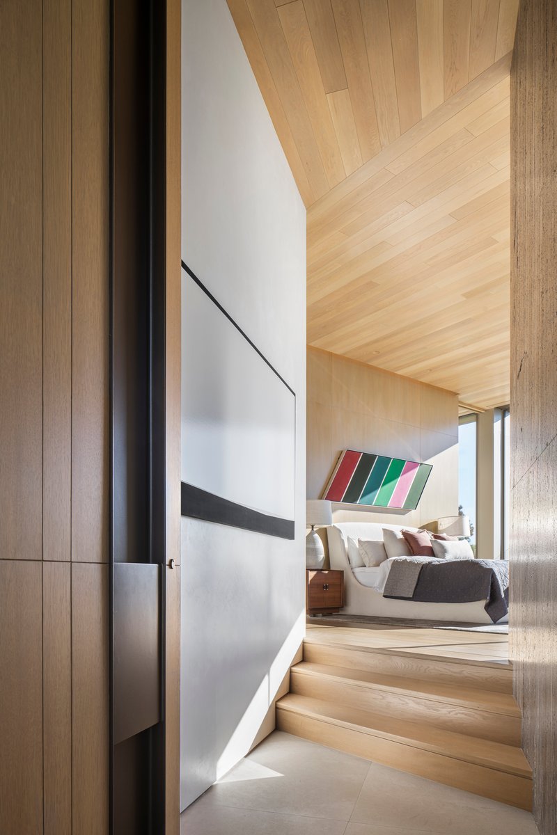 Blonde wood staircase and corridor leading to bedroom with diagonal timber ceiling panels