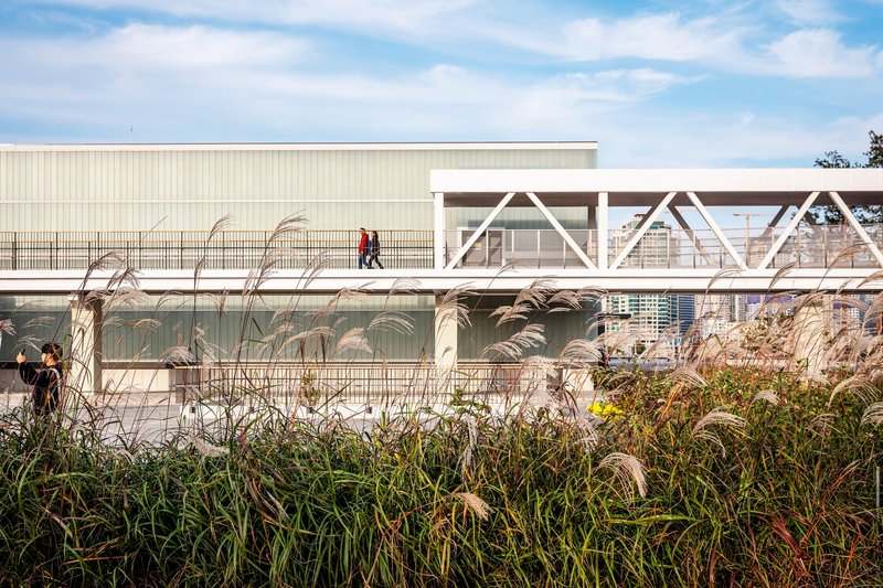 White truss bridge crossing above the corrugated metal building with ornamental grasses in the foreground