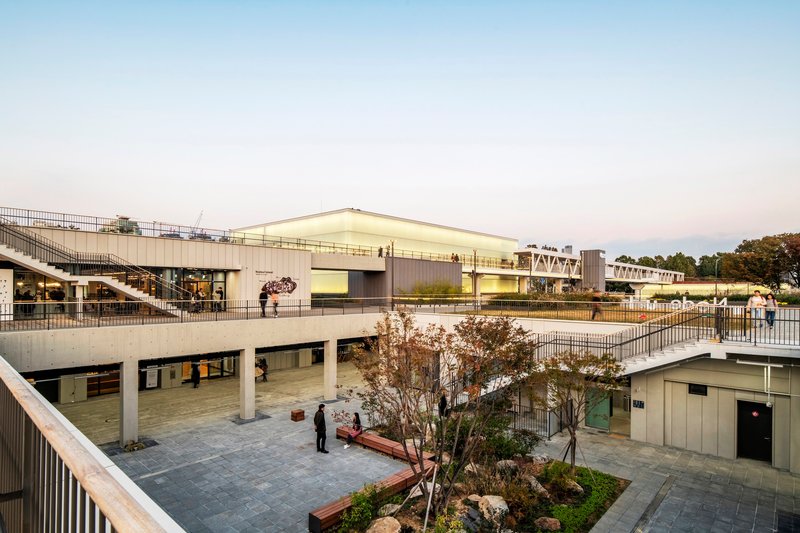 Sunken courtyard with planted beds and timber benches beneath the elevated pedestrian walkways at dusk