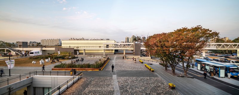 Public plaza with cobblestone paving and an autumn tree between raised transit platforms