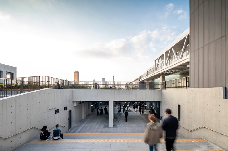 Concrete sunken passageway with pedestrians moving through beneath an elevated walkway