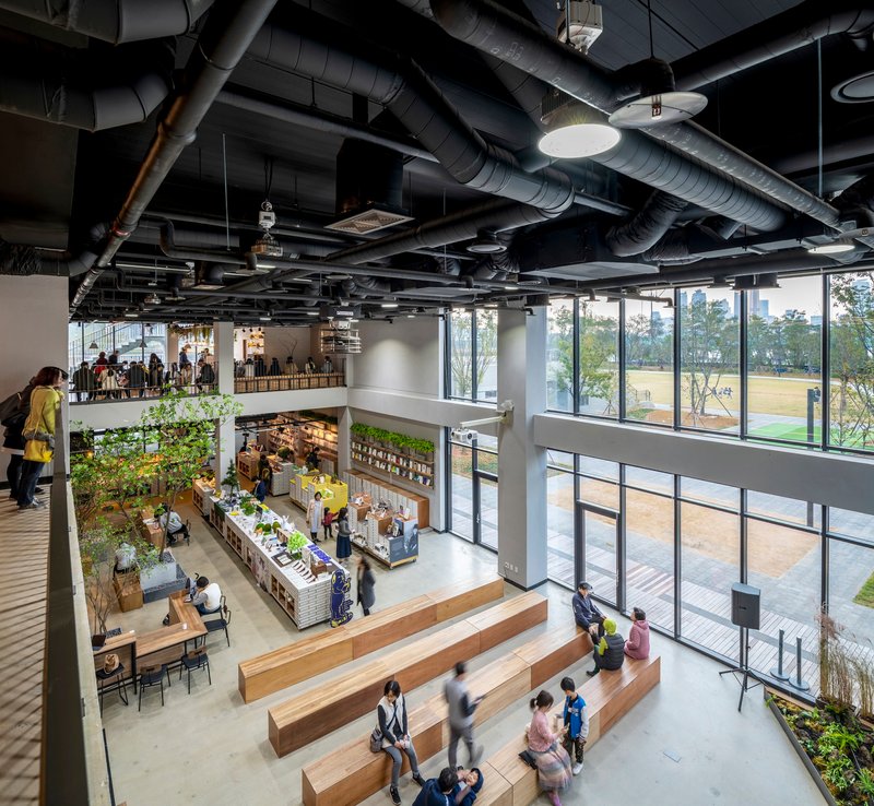 Double-height interior marketplace with timber stepped seating and exposed mechanical systems above