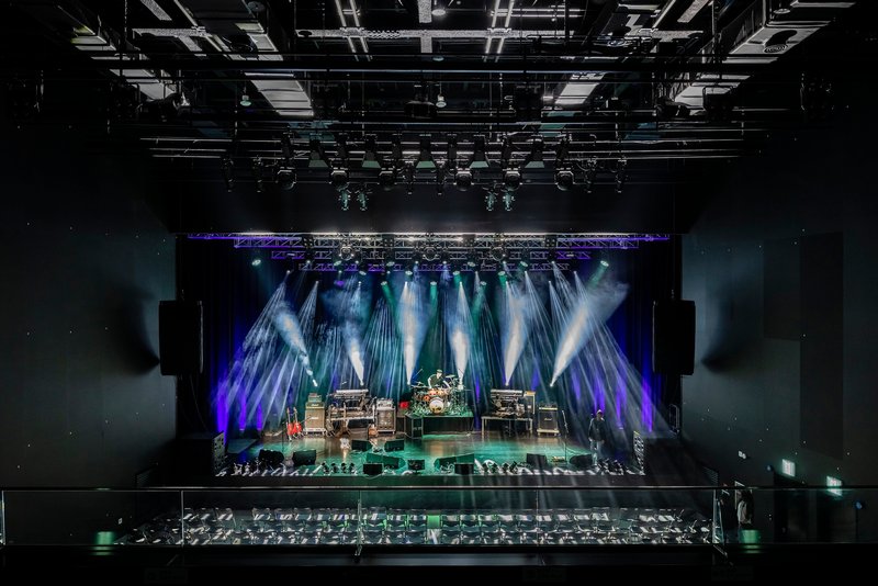 Performance stage rigged with theatrical lighting under a dense grid of exposed mechanical and electrical systems
