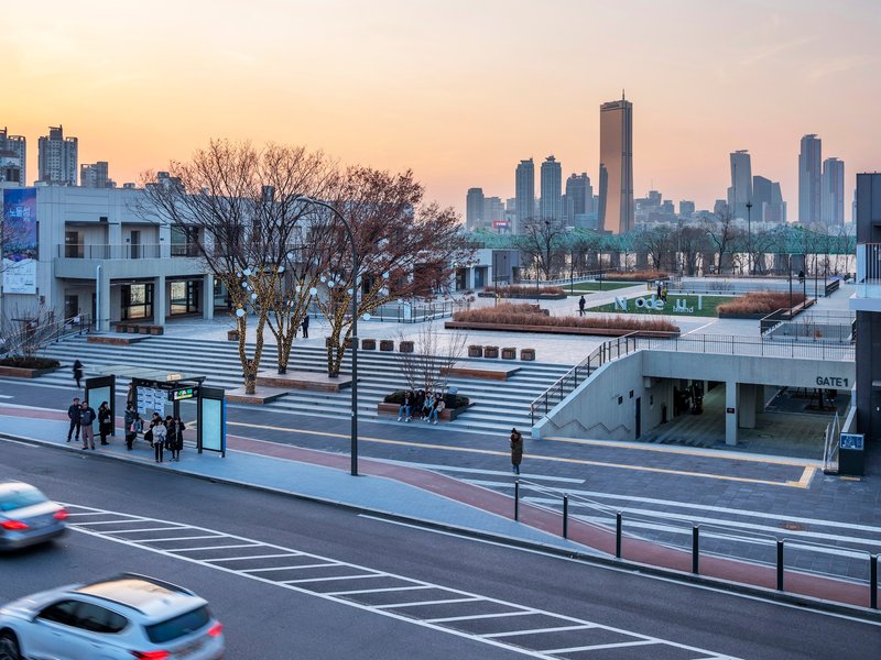 Stepped plaza descending toward planted terraces and bare winter trees with passing traffic in foreground