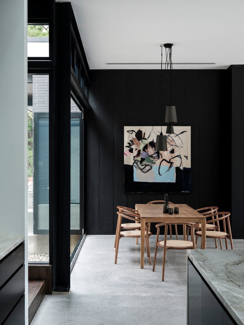 Timber dining table centered beneath black pendant lights with full-height glazing on left wall