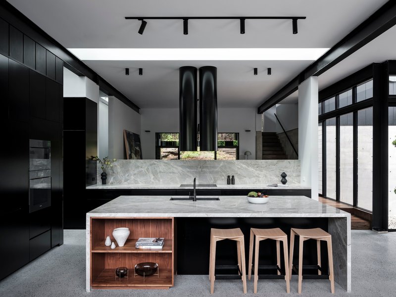Kitchen island with marble waterfall edge and timber shelving nook beneath terrazzo flooring