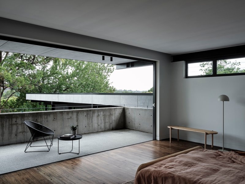 Bedroom opening to concrete terrace with wire chair overlooking leafy canopy