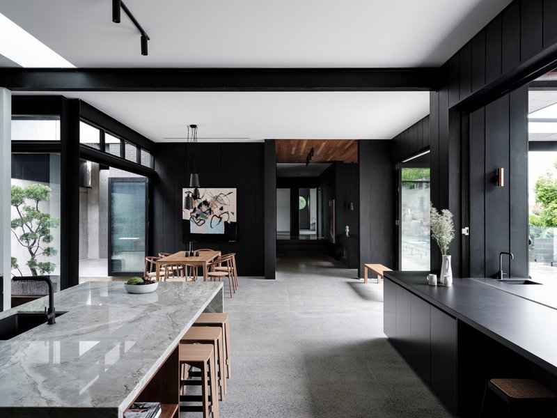 Open-plan kitchen and dining area with black timber walls, marble island, and high clerestory windows