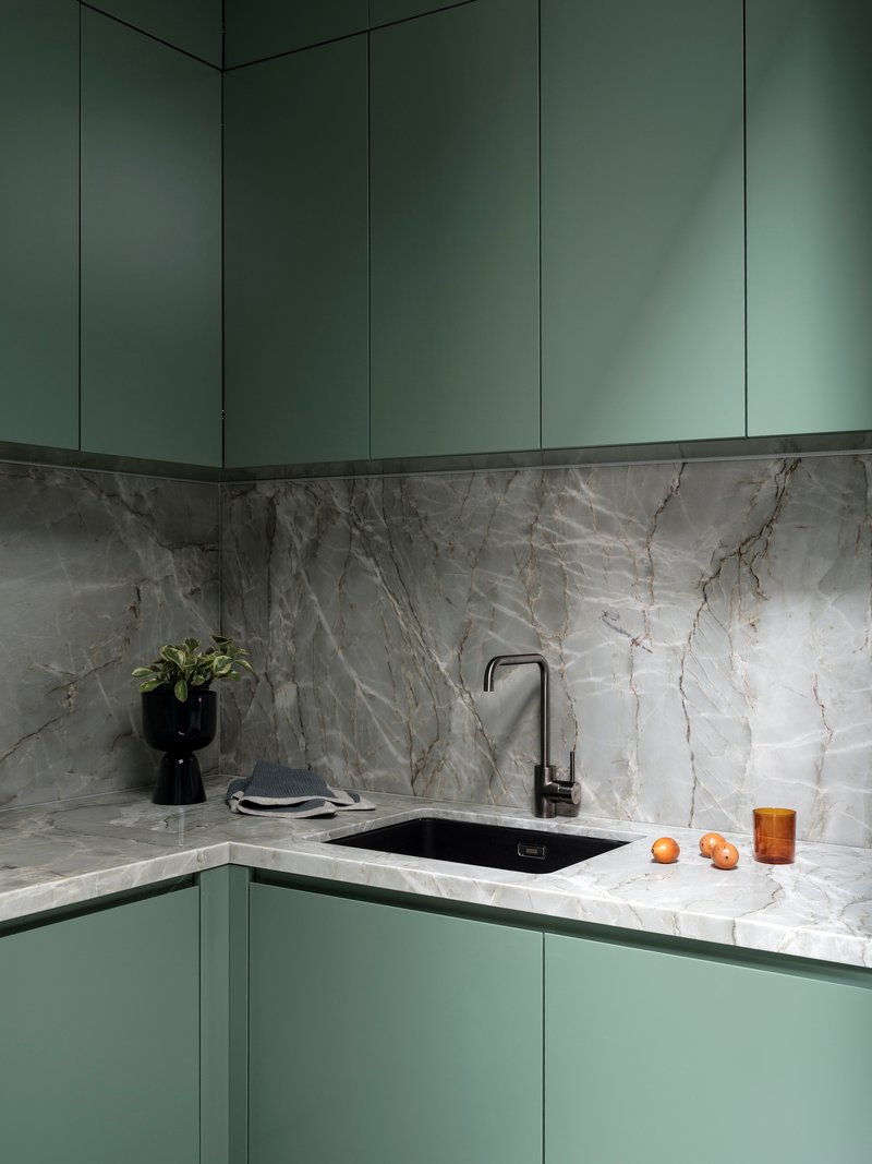 Corner kitchen with sage green cabinetry and grey veined marble backsplash and countertop