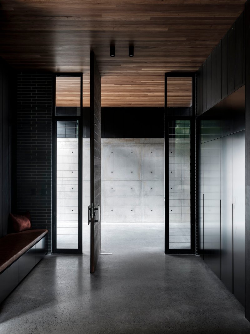 Glass door opening from timber-clad interior hallway to concrete courtyard beyond