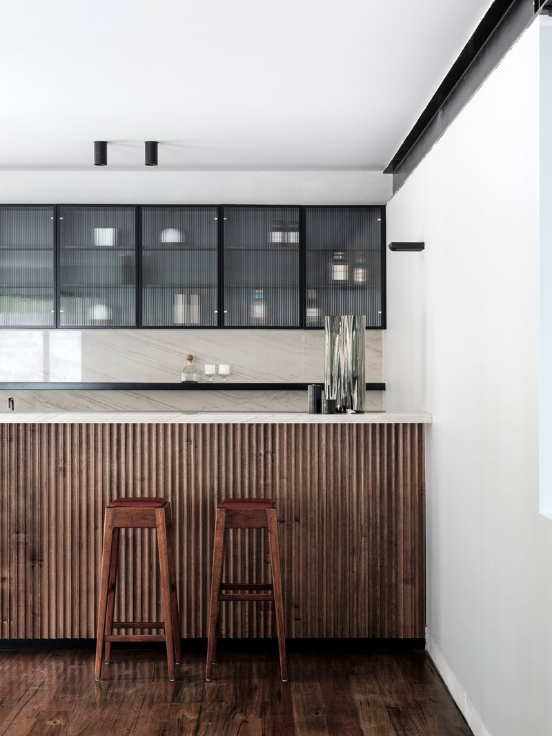 Kitchen island with vertical timber slat cladding and two wooden stools beneath reeded glass cabinets