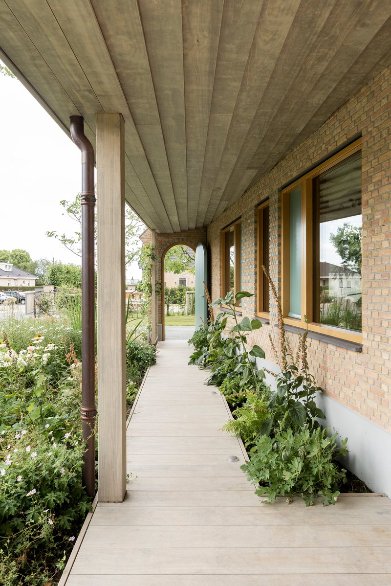 Covered walkway with concrete plank ceiling alongside planted bed and brick wall windows