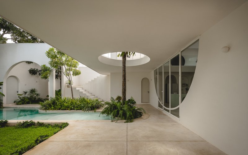 Covered terrace with curved white ceiling and circular skylight overlooking courtyard pool and planted beds