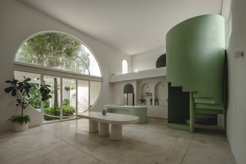 Living space with large circular window, mint green curved staircase, oval table, and courtyard view with potted plants