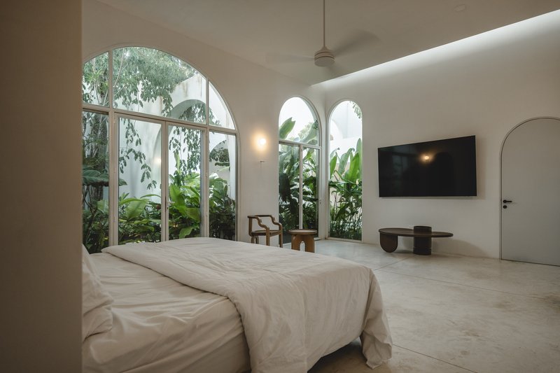 Bedroom with arched windows overlooking a planted courtyard with banana palms in afternoon light