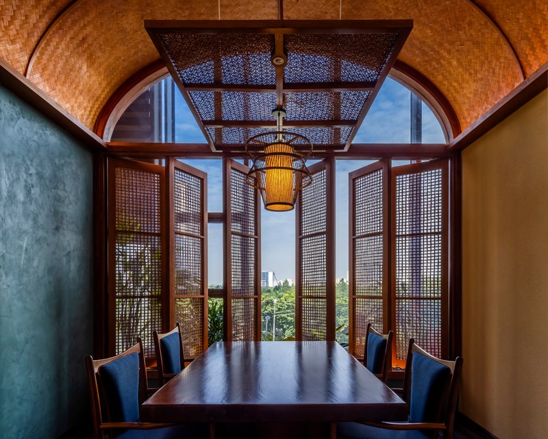 Private dining alcove with woven rattan screens framing a view to greenery through arched openings
