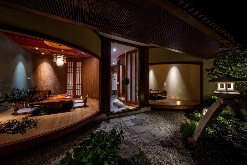 Courtyard view at night showing curved dining room, central corridor, and planted gravel garden with stepping stones